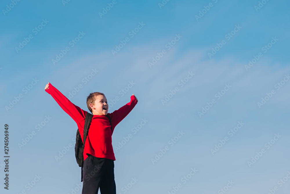 Smiling boy with a backpack behind his back against the sky. Back to school. The boy raised his hands up. Happy student. Smiling boy with a backpack behind his back against the sky. Back to school. The boy raised his hands up. Happy student.
