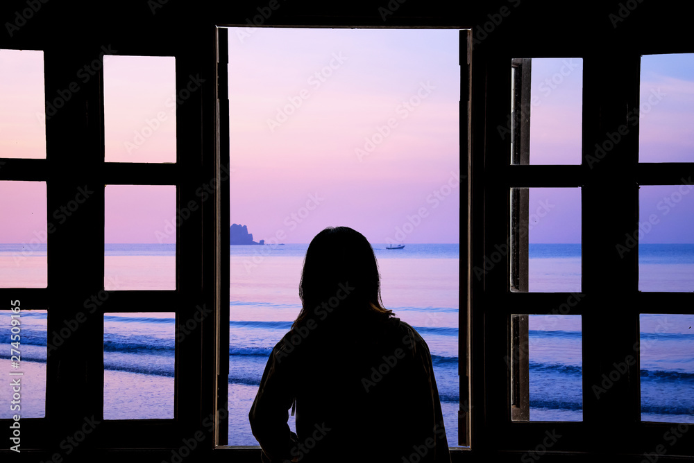 The silhouette of a young woman looking through the window with sea views.