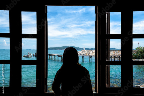 The silhouette of a young woman looking through the window with sea views. © midobun2014