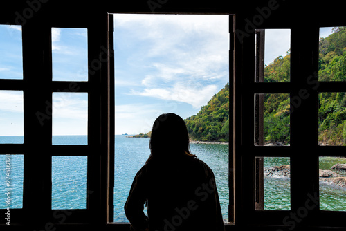 The silhouette of a young woman looking through the window with sea views.