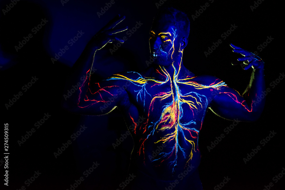 UV patterns body art of the circulatory system on a man's body. On the chest of a muscular athlete, veins and arteries are drawn with fluorescent dyes. The bodybuilder straightened the biceps