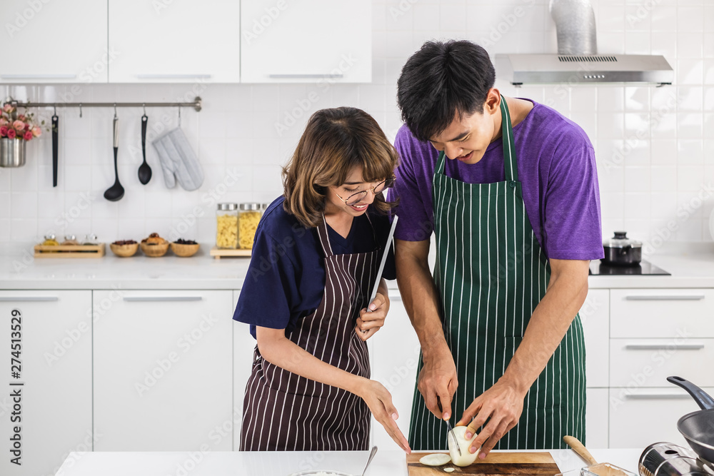 Smiling happy young Asian couple wearing apron and cooking together in ...