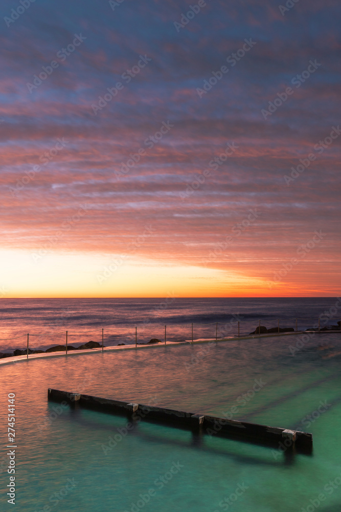 Fototapeta premium Cloudy dramatic sky view over Bronte rock pool at dawn.