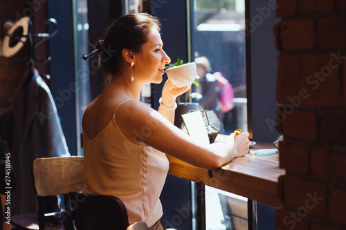 Caucasian romantic woman blogger relaxing drinking tea while sitting near the window in modern loft cafe bar,female freelancer thinking about new ideas during work on laptop computer. Copy space photo