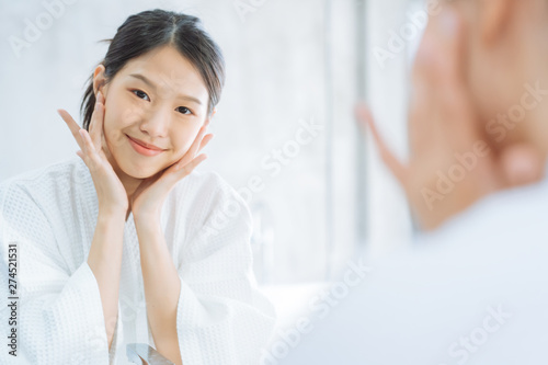 Female Skin Care. Young asian woman touching her face and looking to mirror in bathroom