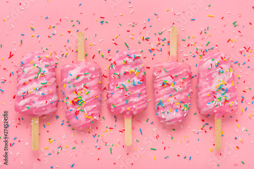 flat lay of creative concept of popsicle with sprinkles and icing over pink b...