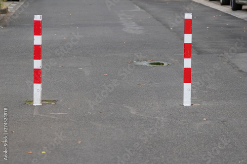Rot weiß gestreifte Pfeiler hindern Autos an der Durchfahrt einer Straße, lassen jedoch Fahrradfahrer passieren und sorgen so für Verkehrsordnung und Verkehrsberuhigung im Straßenverkehr © sunakri