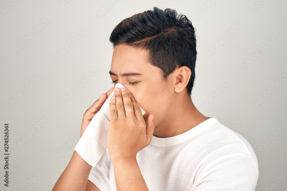 Closeup of sick Asian man blowing nose into tissue, suffering from common cold. Medical and healthcare concept on white background Closeup of sick Asian man blowing nose into tissue, suffering from common cold. Medical and healthcare concept on white background
