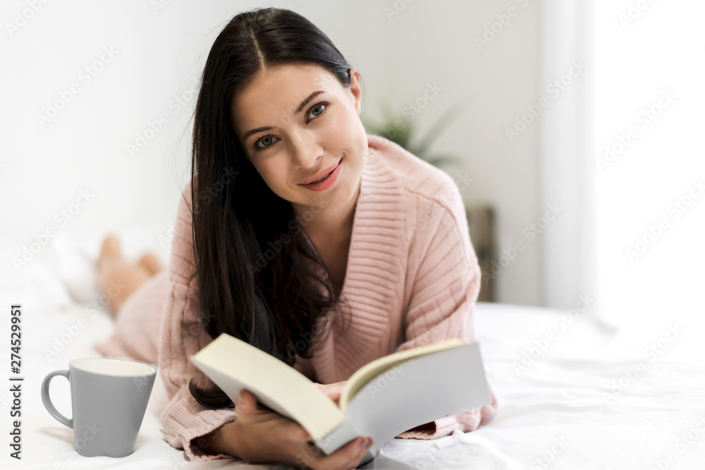 Young woman relaxing and reading book on bed at home Young woman relaxing and reading book on bed at home