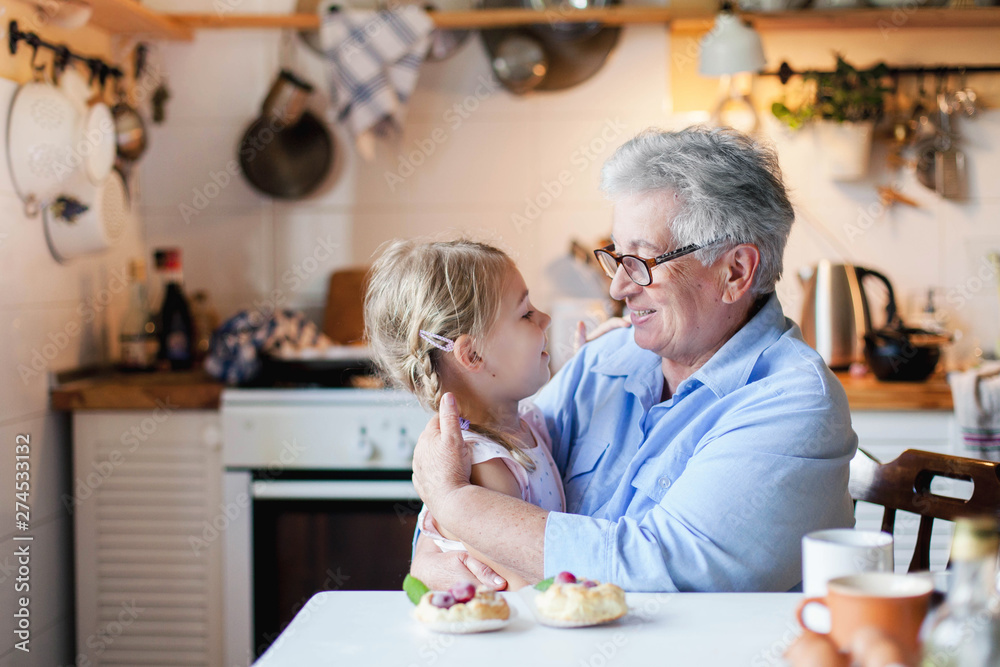 Happy grandmother is hugging granddaughter in cozy home kitchen. Senior woman and cute little child girl are smiling. Kid is enjoying kindness, warm hands, care, support. Family is cooking together. Happy grandmother is hugging granddaughter in cozy home kitchen. Senior woman and cute little child girl are smiling. Kid is enjoying kindness, warm hands, care, support. Family is cooking together.