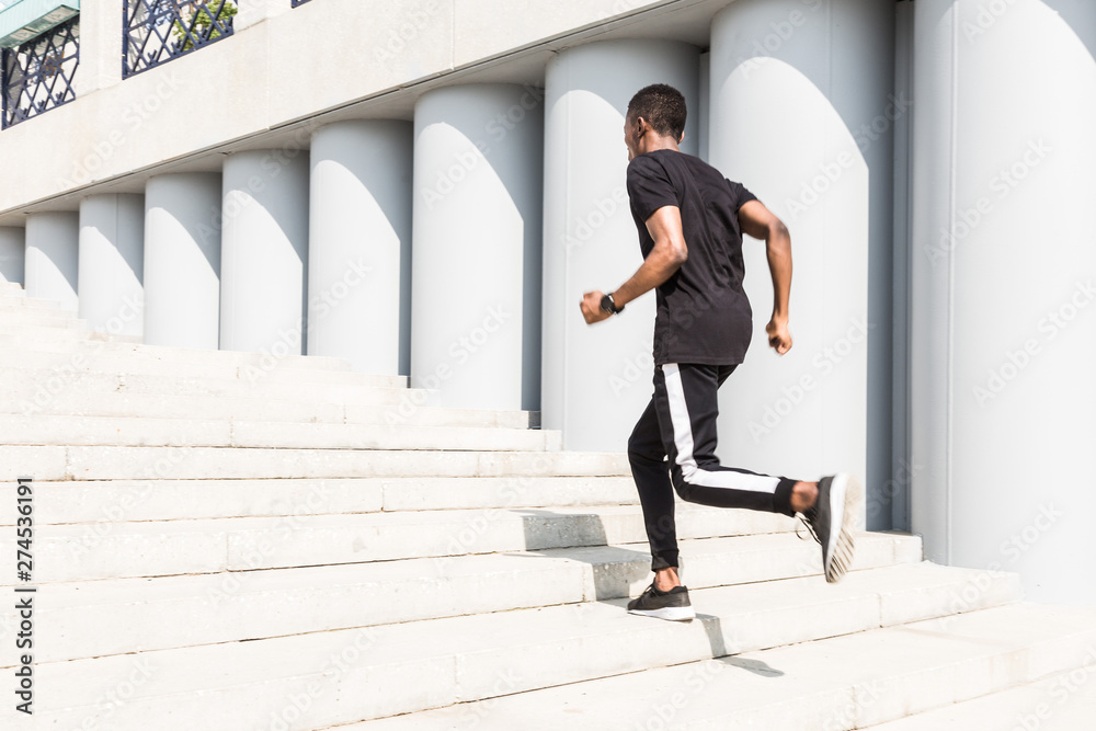 Fototapeta premium Athletic young afroamerican man running on the promenade. Black Male runner sprinting outdoors. Healthy lifestyle concept.