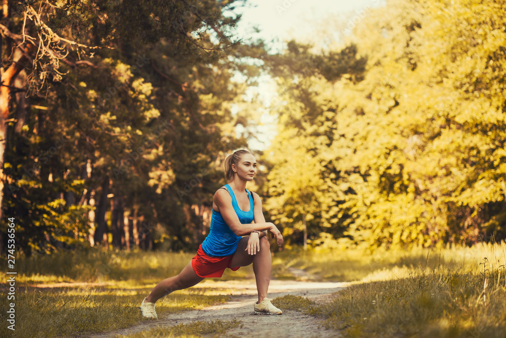 Pretty woman athlete doing exercises before jogging through the summer forest