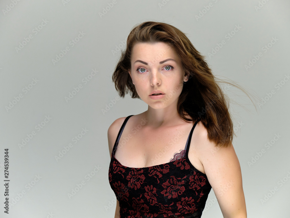 Closeup portrait of pretty girl, brunette woman 30 years old on a light gray background with beautiful dark hair and excellent skin of the face and body. She shows emotions, smiles, wonders.