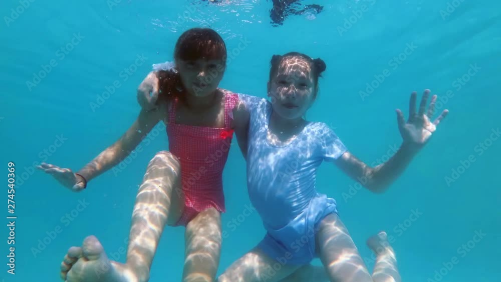 Two cute little girls hug and pose for the camera underwater at the