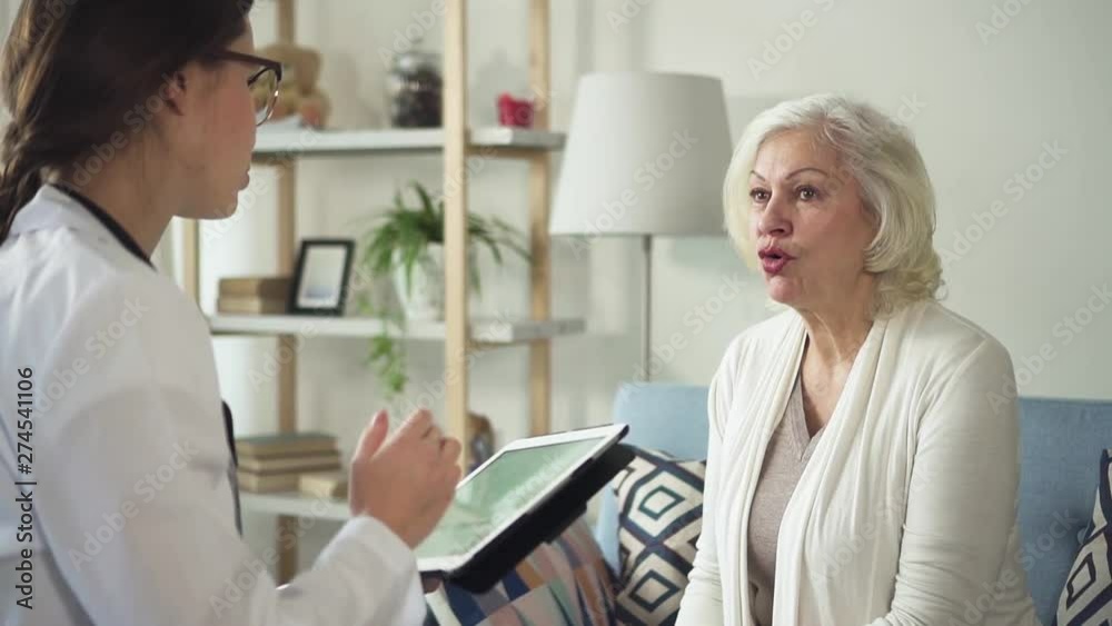 Senior patient is talking with neurologist and discussing about illness symptoms. Confident medical specialist in uniform is listening and checking all by laptop.Mature woman is smiling while Senior patient is talking with neurologist and discussing about illness symptoms. Confident medical specialist in uniform is listening and checking all by laptop.Mature woman is smiling while