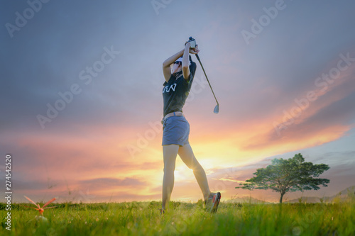 woman golf player in action setup address after hit the golf ball away from fairway to the destination green off, fairway at light of sunset in background