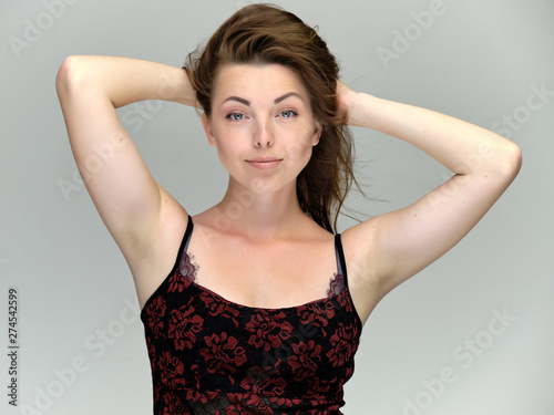 Closeup portrait of pretty girl, brunette woman 30 years old on a light gray background with beautiful dark hair and excellent skin of the face and body. She shows emotions, smiles, wonders.