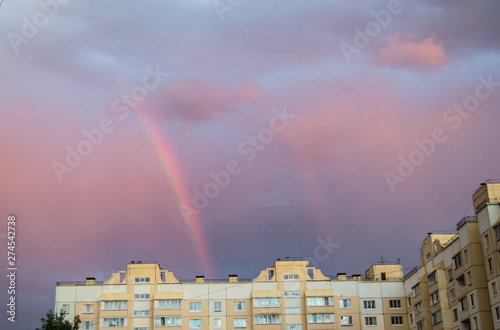 Rainbow over the roof of a multi-storey city house in the evening pink sunset sky after the rain, summer fantastically beautiful magical landscape photo