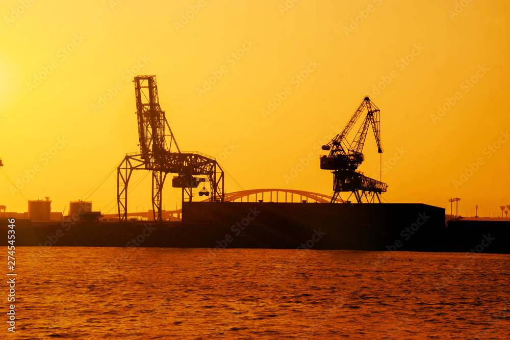 Silhouette of container crane at Osaka port are loading on evening with sunset color tone and gantry crane working background.