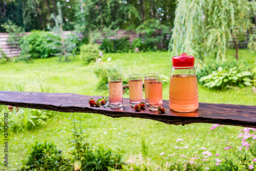 Long wooden table with four full glasses and jug of fruit juice, strawberries and mint. Summertime in countryside.