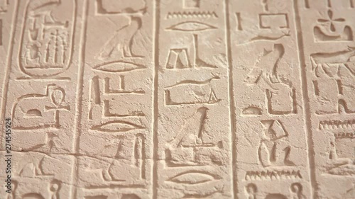 Ancient Egyptian hieroglyphic carvings on a temple wall in Luxor Egypt, CGI tilt up shot, shallow depth of field.