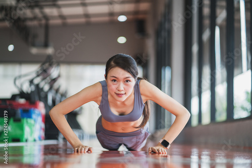 Beautiful Asian woman doing push ups in the gym before lifting some weights.