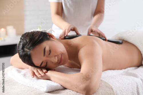 Beautiful Asian woman getting hot stone massage in spa salon
