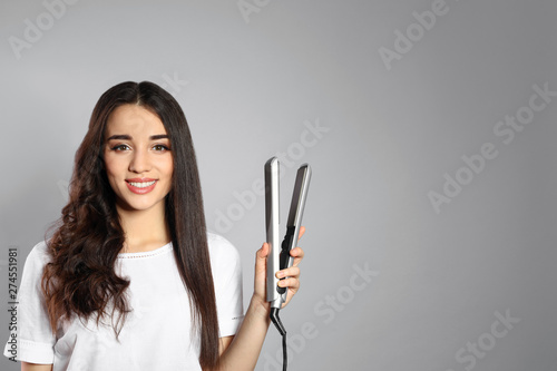 Happy woman with hair iron on grey background. Space for text