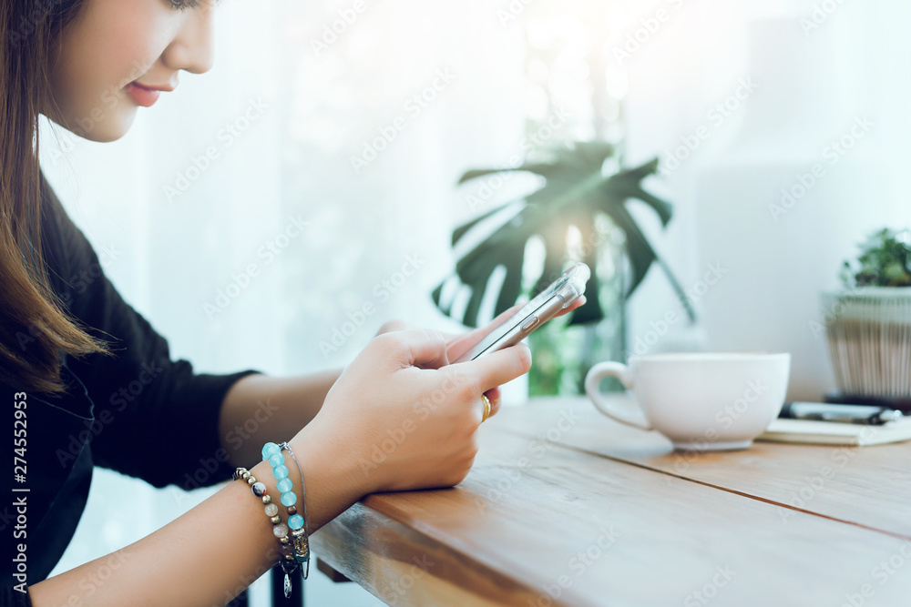 Fototapeta premium Closeup of hand young beautiful woman using smartphone to working or shopping online in cafe with cup of coffee on wooden table