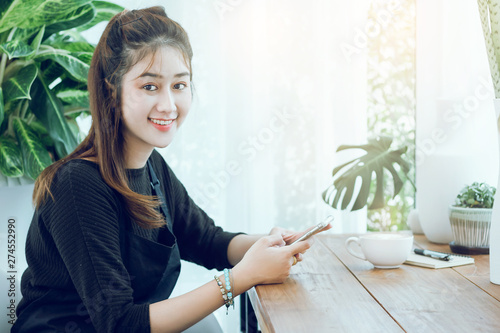 Portrait of young beautiful woman using smartphone to working or shopping online in cafe with cup of coffee on wooden table