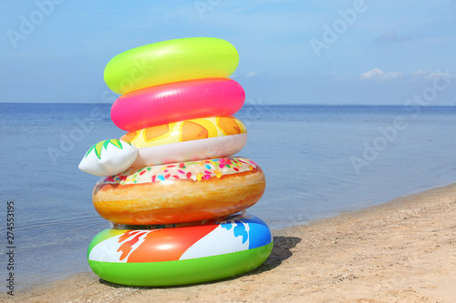 Stack of different bright inflatable rings on sandy beach near sea. Space for text