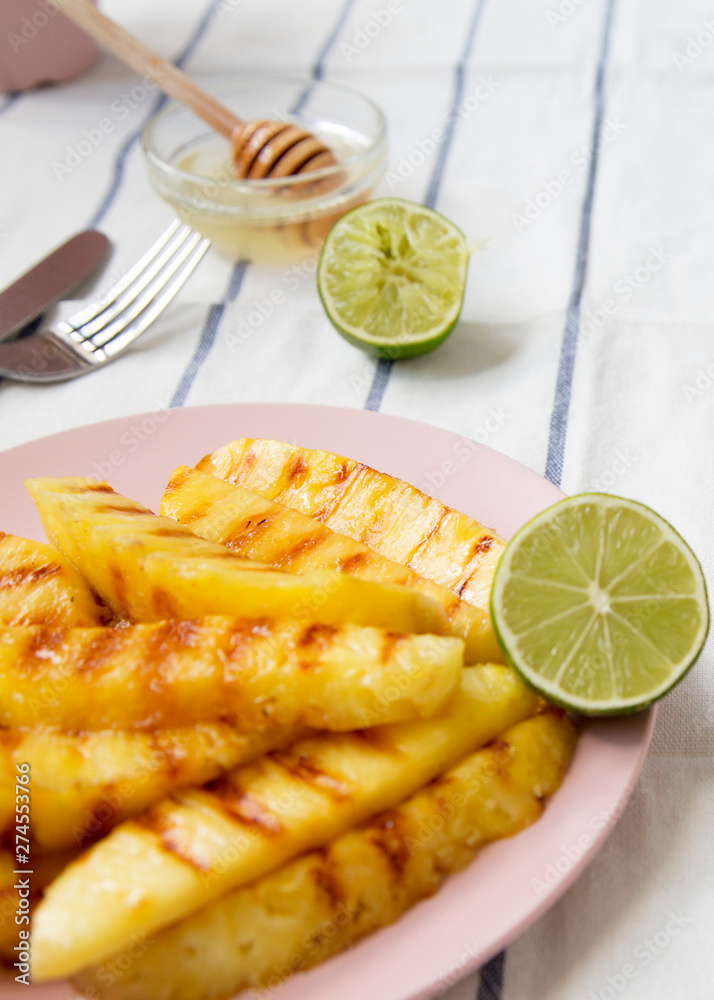Grilled pineapple slices on a pink plate with honey and lime, low angle. Summer food. Close-up. Selective focus.