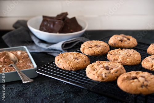 Cookies with chocolate chips and hazelnuts, on metal grill, made with oatmeal and wheat flour. Accompanied with chocolate powder and chocolate with almonds.