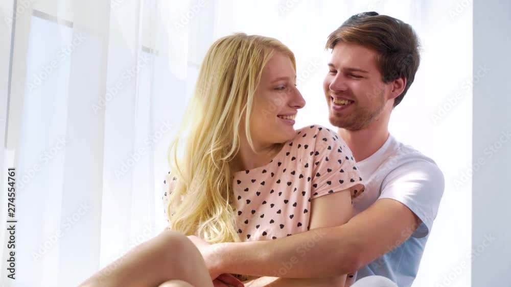 young lovely couple hugging near curtained window in morning sunshine young lovely couple hugging near curtained window in morning sunshine