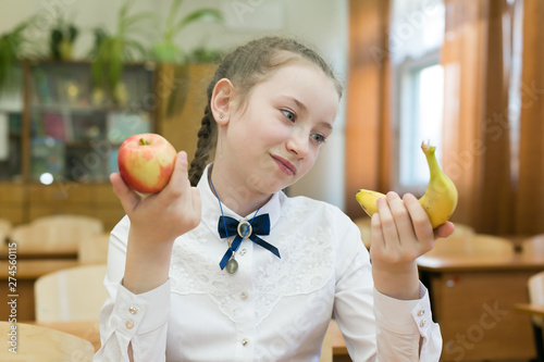 Girl in school uniform chooses food for lunch. School girl on a diet makes a choice between fruit and a harmful sandwich. photo