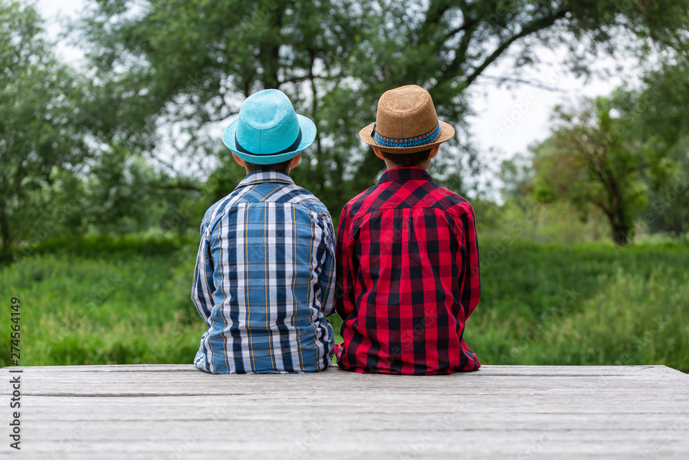 Dreamy brothers sitting on a wooden pier by the river.