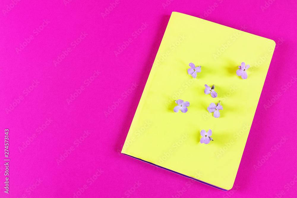 Bright lime notebook and lilac flower on a bright pink background. Place for text. The concept of learning, sketch, herbarium. Flat lay, minimalism, top view, design.