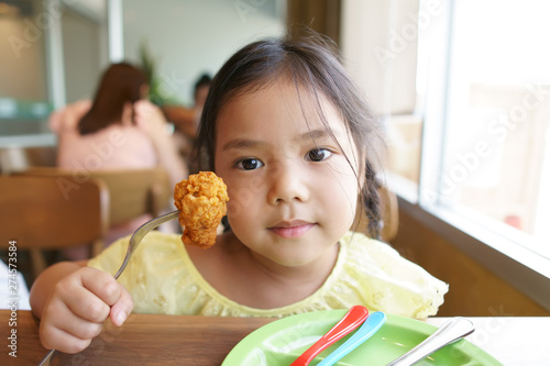 Asian child hungry or kid girl enjoy eating food with smile and holding fried chicken calves on fork and dish for delicious and happy for lunch or breakfast in morning at restaurant or food court
