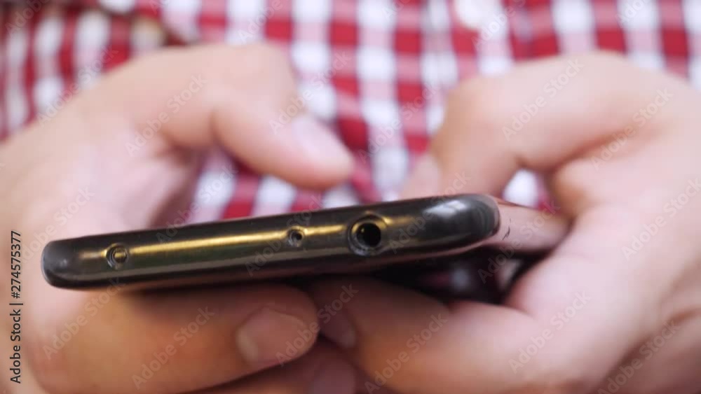 A man in a white red checkered shirt is using a smartphone while typing a message or writing an electronic mail A man in a white red checkered shirt is using a smartphone while typing a message or writing an electronic mail