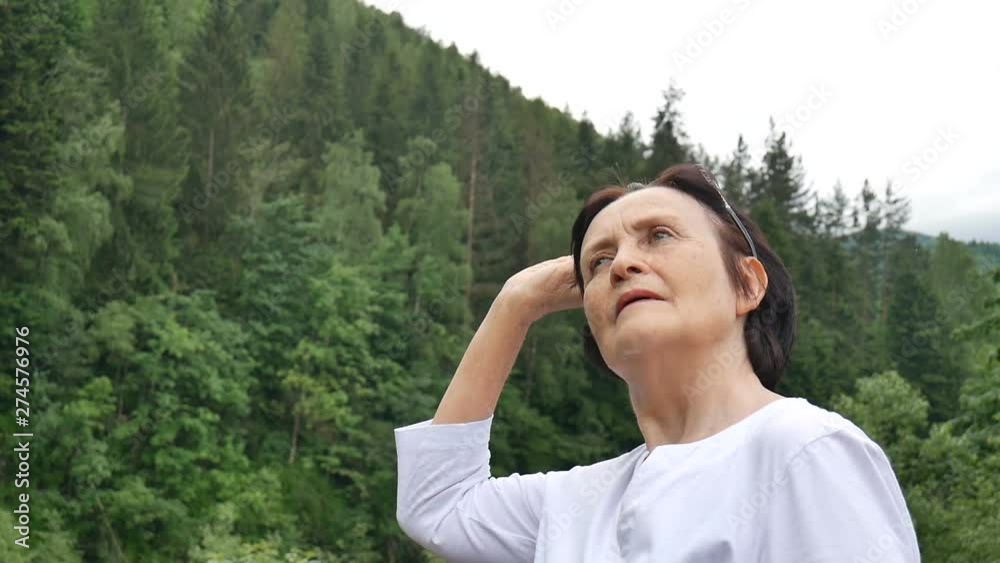 Portrait of a happy relaxed pensioner on vacation in the mountains. Woman takes off sunglasses and looks into the distance. Fresh mountain air, travel concept, Mother's Day Portrait of a happy relaxed pensioner on vacation in the mountains. Woman takes off sunglasses and looks into the distance. Fresh mountain air, travel concept, Mother's Day