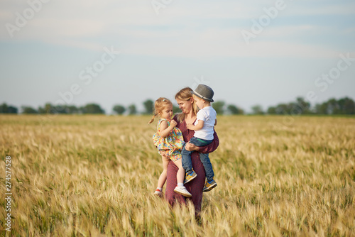 Family values. Happy young mother and her children spending time together in sunny field. Mom hugging and loving her little kids. Care concept