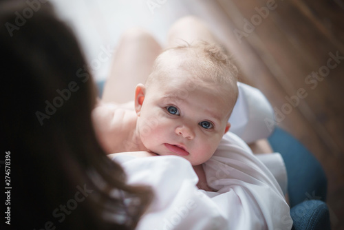 A young mother in white shirt holds the baby in her hands and breastfeeds. Close up newborn looks directly into the camera
