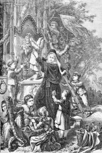Holy Mary celebration as queen of May: a nun with the help of little girls and boys decorates a small chapel with flower festoons and a crown