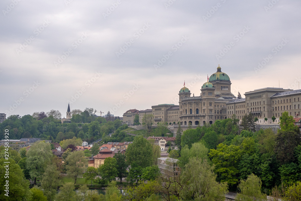 The Bundeshaus, parliament in bern , switzerland, with green trees foreground and cloudy sky background