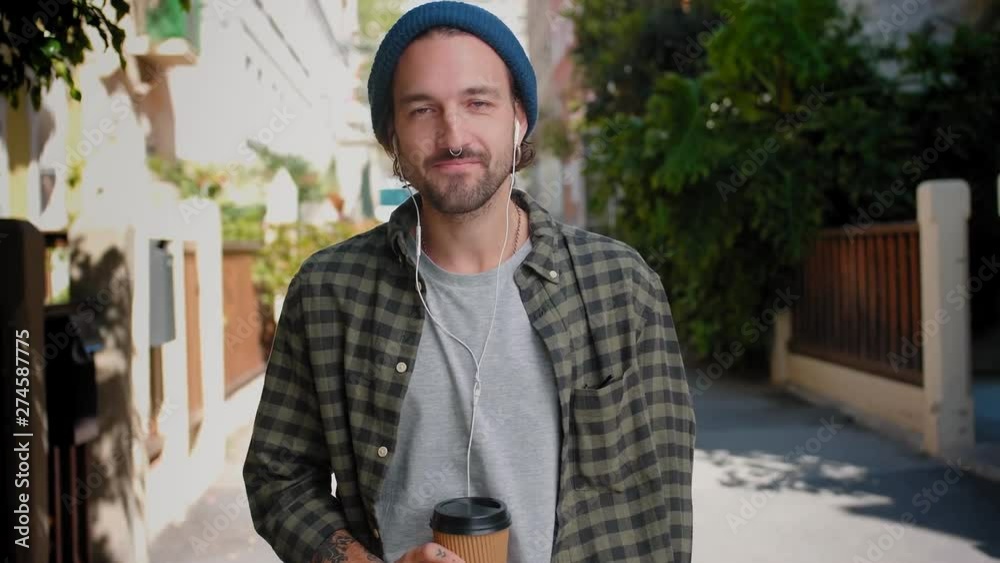 Portrait of handsome man drinking tasty coffee standing outdoor and smiling with earphones, casual Hispanic male enjoying sunny day at city street and listening joyful music, dressed in blue hat and Portrait of handsome man drinking tasty coffee standing outdoor and smiling with earphones, casual Hispanic male enjoying sunny day at city street and listening joyful music, dressed in blue hat and