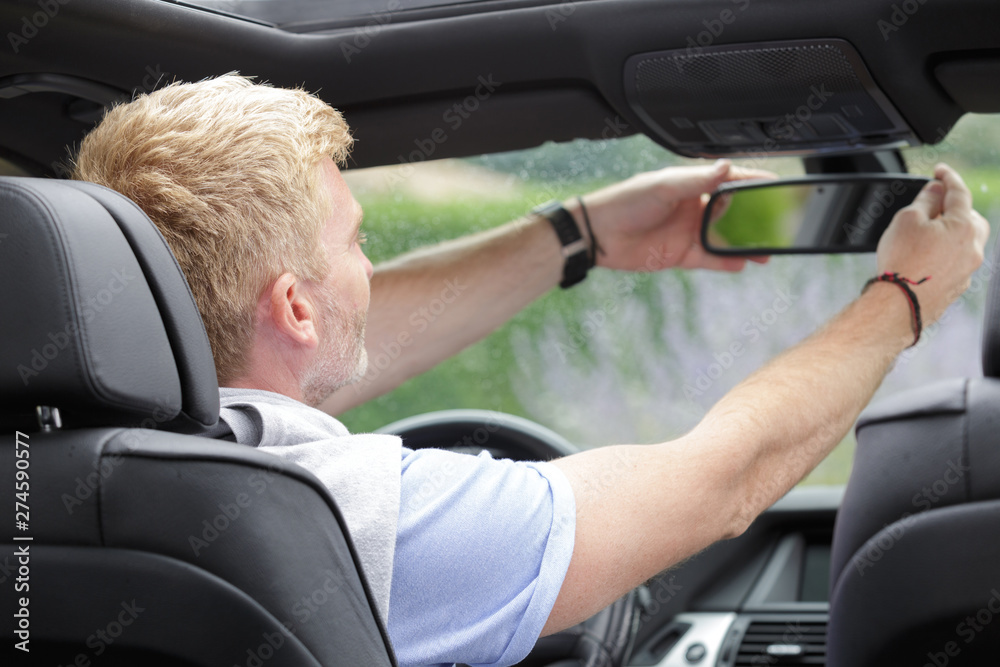 middle-aged male driver adjusting rear view mirror in car middle-aged male driver adjusting rear view mirror in car