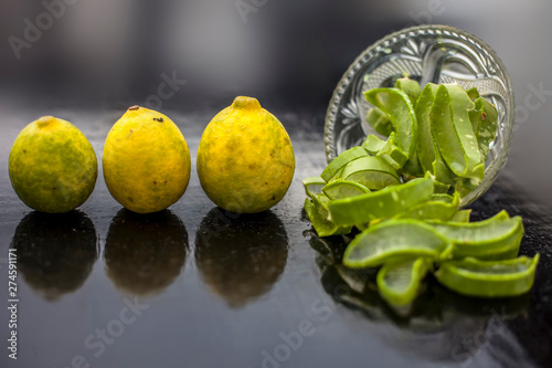 Raw cut aloevera or aloe vera gel in a glass bowl and some fresh ripe lemons or limbu or nimbo on wooden surface along with their reflection on the surface. photo