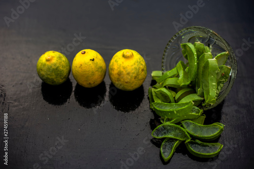 Raw cut aloevera or aloe vera gel in a glass bowl and some fresh ripe lemons or limbu or nimbo on wooden surface along with their reflection on the surface. photo