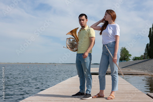 The guy playing the horn and the girl playing the flute on the lake
