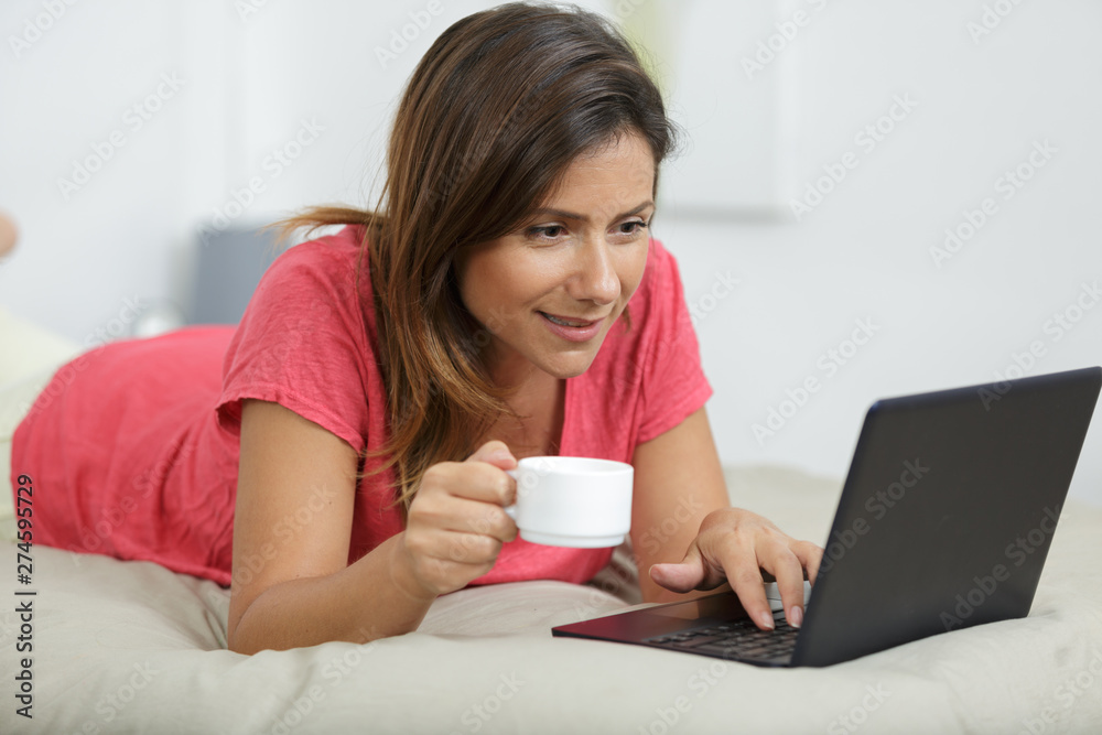 woman layed on bed using notebook computer woman layed on bed using notebook computer